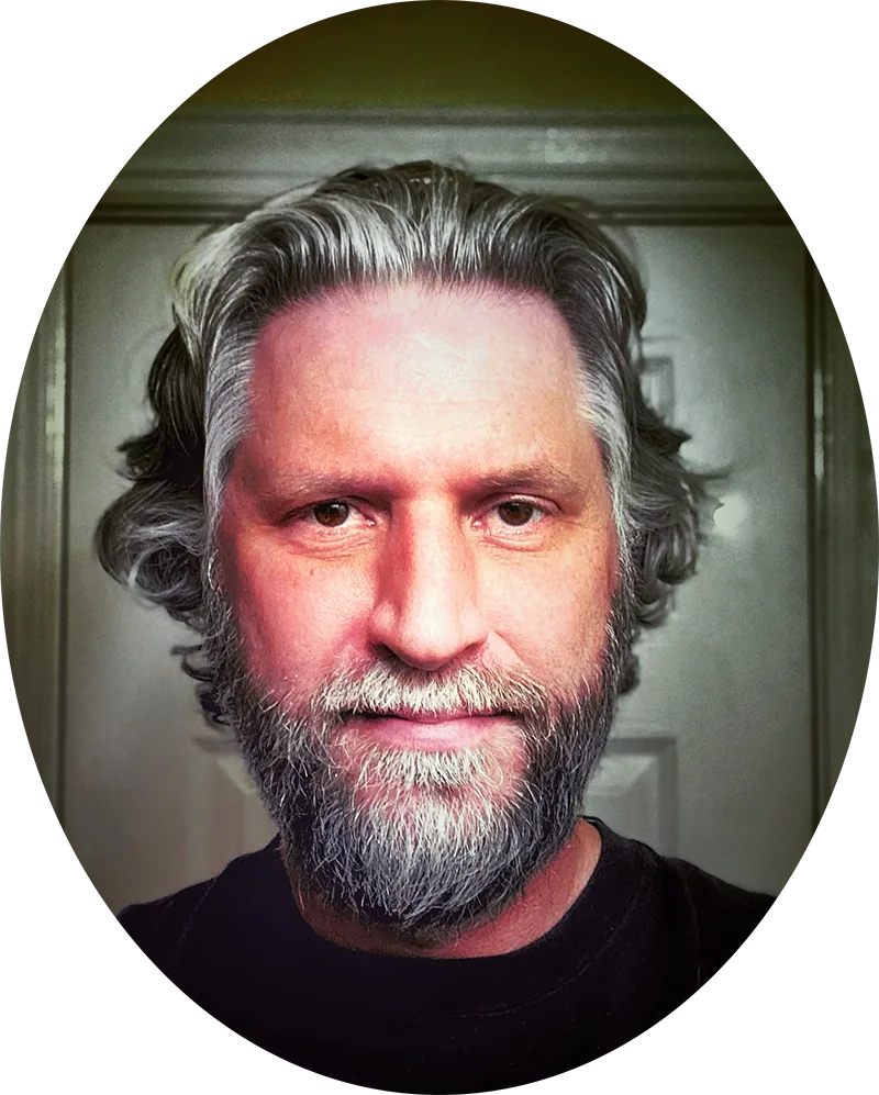 Oval portrait of Jeff with grey hair and a full beard, looking directly at the camera.