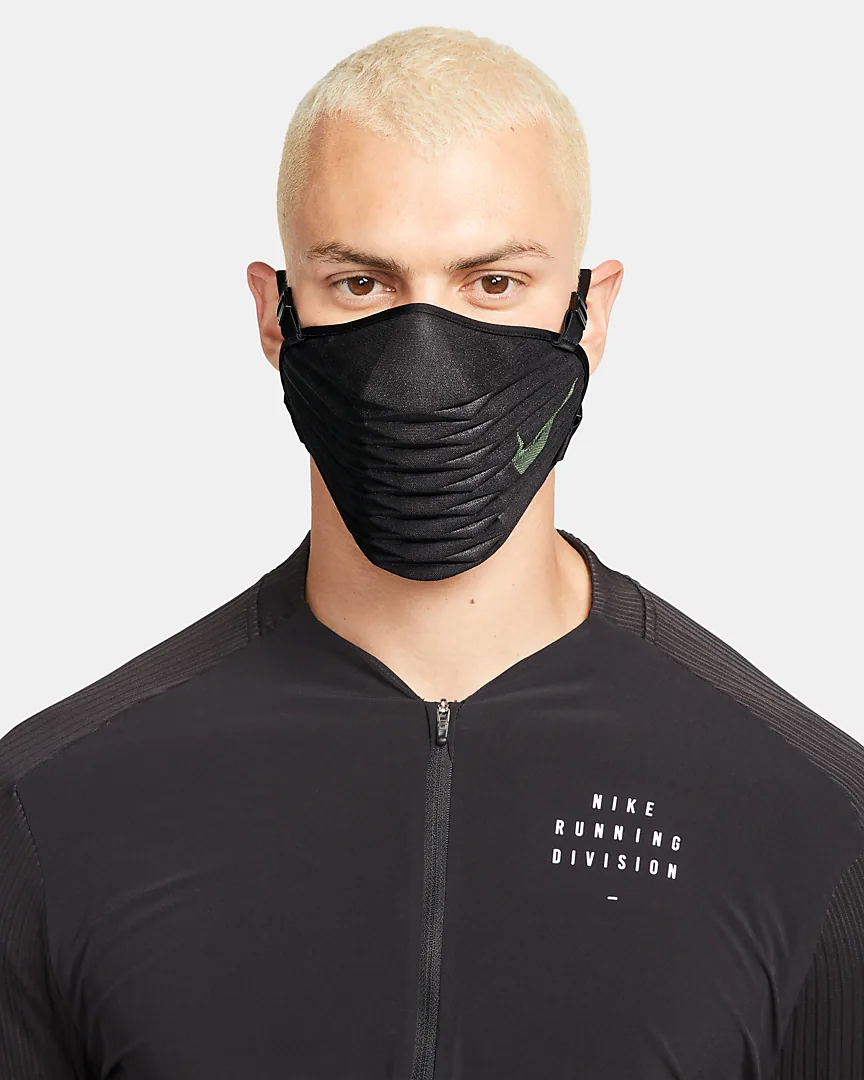 A person wearing a black pleated performance face mask with adjustable straps hooked over the ears.